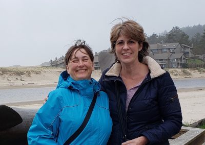 Two girlfriends smiling with beach in the background