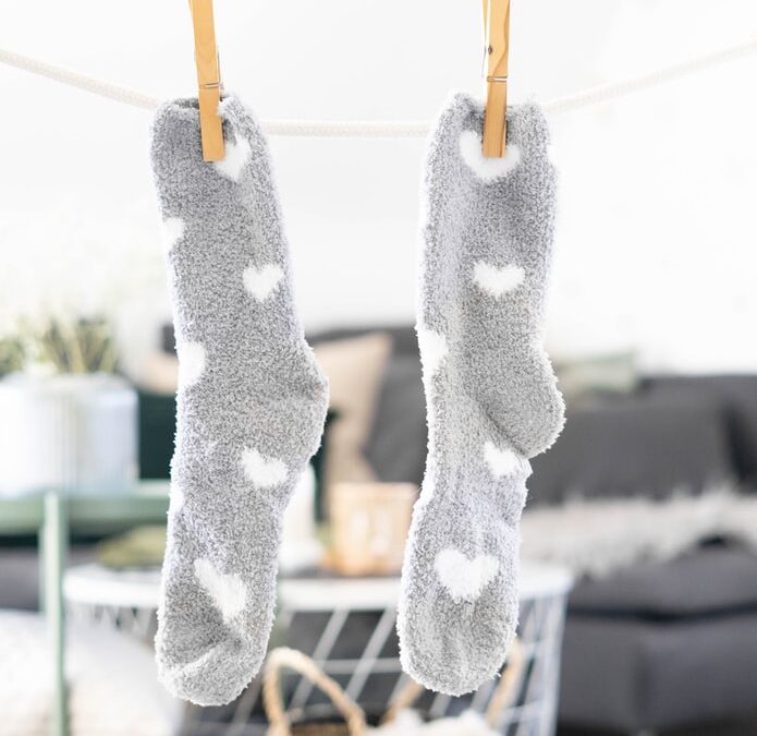 Gray socks with white hearts hanging from brown wood clothes pins