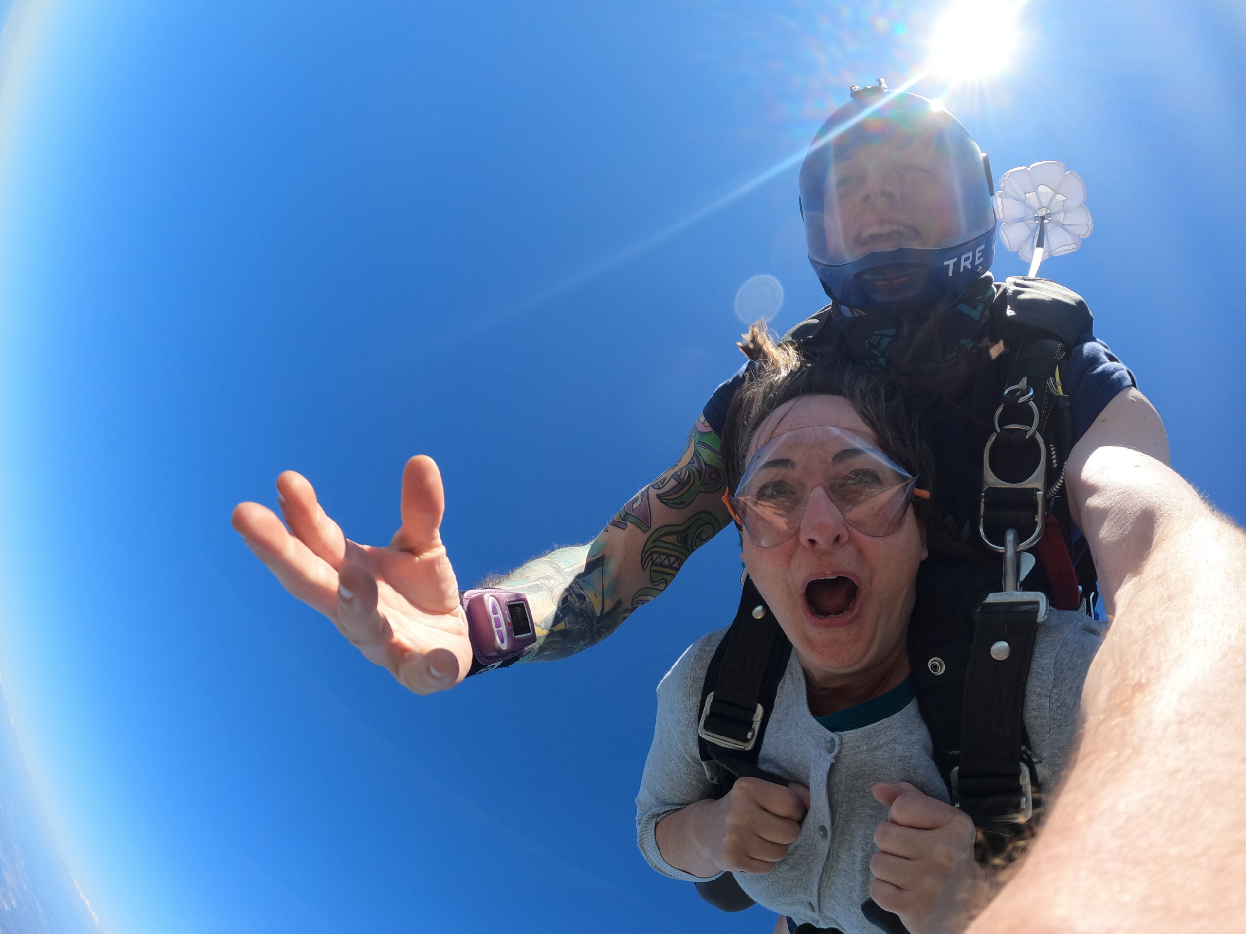 Guy and gal tandem skydiving with blue sky background.