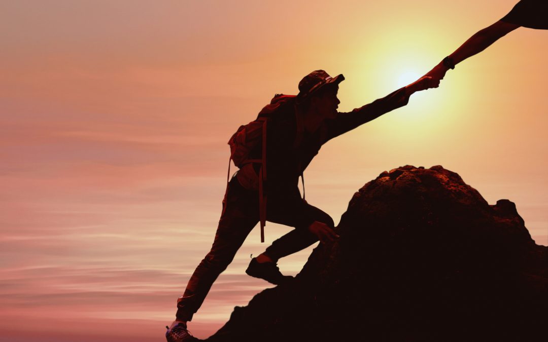 silhouette of man climbing up mountain with helping hand